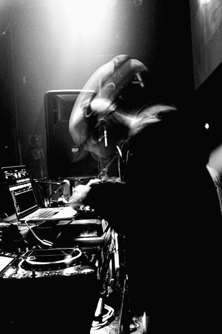 A DJ in a hood, lit from behind, playing